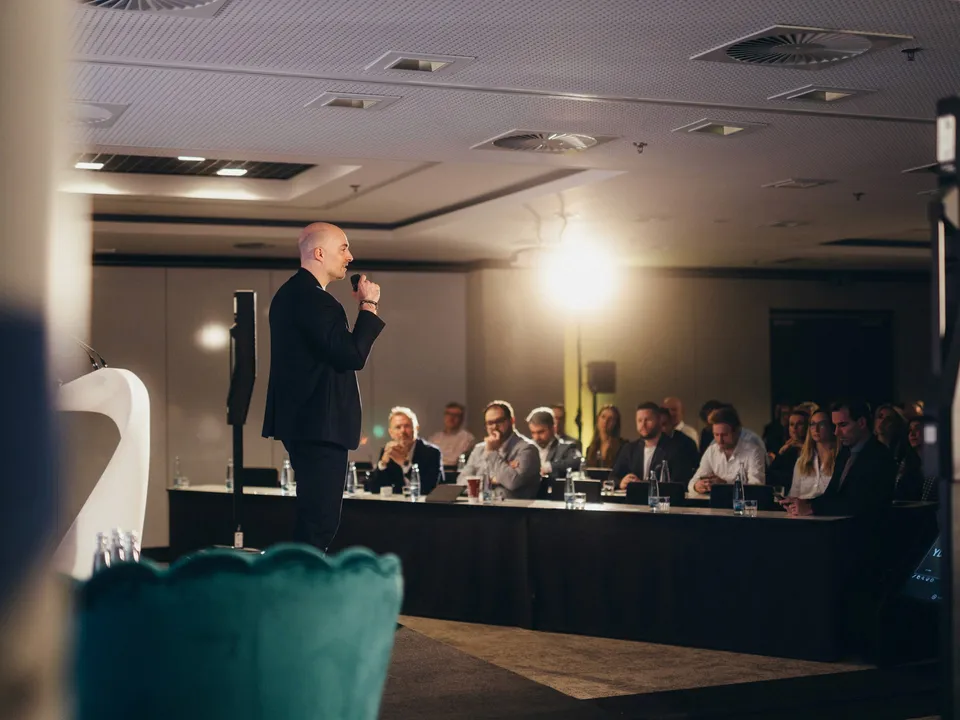Řečník s mikrofonem před publikem na firemní konferenci